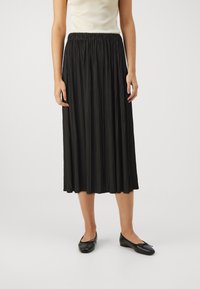 Svart plisserte skjørt med elastisk midjebånd, midi-lengde, laget av lett stoff, kombinert med svarte flate sko. Enkelt design, ingen pynt.