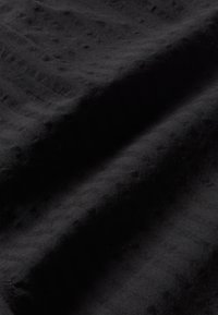 Tissu noir avec un motif texturé et ondulé. Surface douce et légèrement pelucheuse, affichant une teinte profonde et une coloration uniforme.