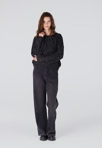 Zwarte textured trui met glitters, losse pasvorm, brede lange mouwen; gecombineerd met hoge zwarte jeans en chunky zwarte boots.