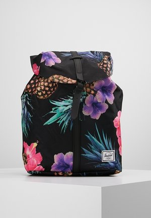 Sac à dos noir avec imprimé ananas tropical et fleurs colorées, sangle à boucle à l'avant, et petite étiquette de marque blanche près du bas.