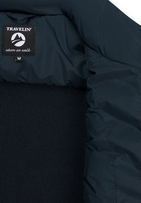 Marineblauwe jas met een zwart label waarop "TRAVELIN' where we walk" staat en een maatlabel gemarkeerd met "M" op de gebreide stof aan de binnenkant van de kraag.