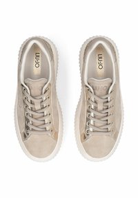 Paire de baskets en daim beige avec semelles blanches à rainures, lacets beige, accents métalliques dorés et semelles intérieures de marque visibles vue de dessus.