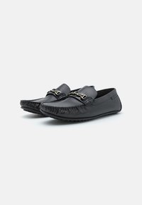 Schwarze Lederloafers haben eine abgerundete Spitze, gestickte Details und eine goldfarbene Hardware-Akzentuierung auf dem Obermaterial. Strukturierte Sohle für besseren Halt.