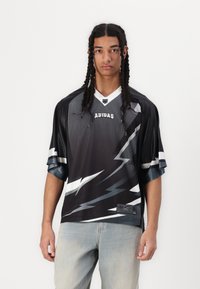 Black and gray jersey with lightning bolt print, short sleeves, mesh texture, and Adidas logo. Worn with light blue jeans.