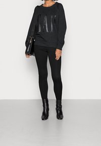 Sweat-shirt à imprimé léopard noir avec le logo "GAP", leggings noirs et bottines noires. Le mannequin porte un sac à bandoulière noir.