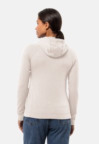 Lichtbeige hoodie met lange mouwen, raglan naden en een gladde textuur. Gecombineerd met blauwe denim jeans, wat een casual look laat zien.