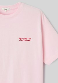 T-shirt en coton rose clair avec manches courtes, col rond et texte brodé rouge "COURIR POUR LES MEILLEURS CRÊPES" sur la poitrine gauche.