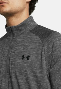 Half-zip athletic jacket made of textured gray fabric with black accents. Features a small black logo on the chest and contrasting shoulder design.