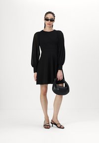 Must mustriga, puffed sleeves'id, sobiv kehaosa ja laienev seelik. Kaunistatud musta käekotiga ja tumedate prillidega, kantud sirtsutavate kontsadega.