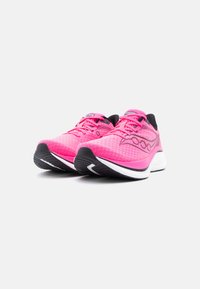 Ζευγάρι λαμπερά ροζ αθλητικά παπούτσια Saucony με μαύρες και άσπρες σόλες πάνω σε λευκό φόντο, τοποθετημένα έτσι ώστε να φαίνονται οι λεπτομέρειες από μπροστά και από το πλάι.