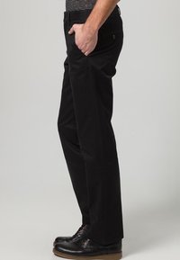 Pantaloni neri realizzati in tessuto liscio, con una vestibilità dritta, tasche frontali e una tasca posteriore con bottone. Indossati con scarpe nere.