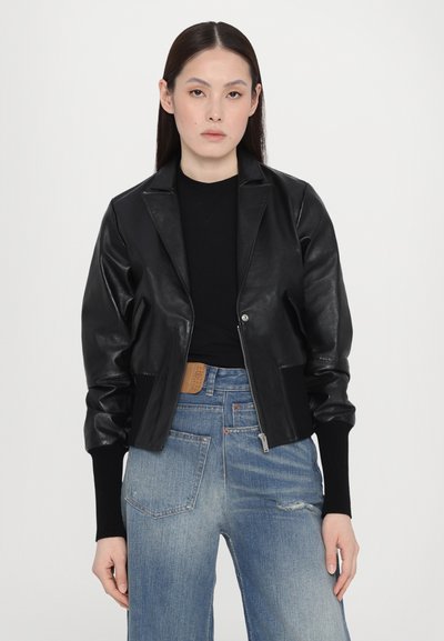Black leather cropped jacket with a shawl collar, silver zipper, ribbed cuffs, and a smooth, glossy texture. Worn over a black top.