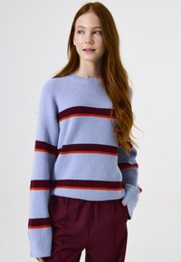 Helles blaues Strickpullover mit horizontalen Streifen in tiefrot und orange. Verfügt über einen Rundhalsausschnitt und lange, weite Ärmel.