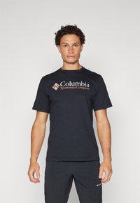 Černé tričko s krátkým rukávem vyrobené z jemné látky, s výrazným červeným a bílým logem společnosti Columbia Sportswear Company na přední straně.