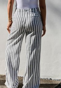 Pantalons larges à rayures grises et blanches en tissu léger. Comprend une poche arrière et une taille haute. Texture lisse, design fluide.