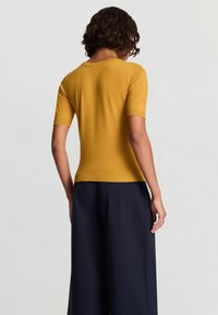 Mustard yellow fitted knit top with short sleeves, a round neckline, and ribbed hem, worn with loose navy wide-leg pants.