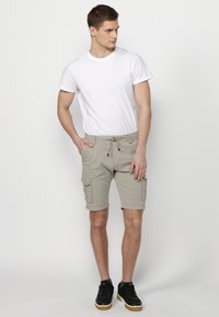 Helle beigefarbene Cargo-Shorts mit mehreren Taschen, elastischem Bund mit Kordelzug, kombiniert mit einem schlichten weißen T-Shirt und schwarzen Sneakers.