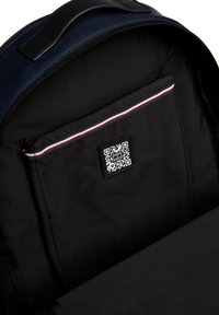 Interno di uno zaino navy con foderatura in tessuto liscio, dotato di una tasca nera con un codice QR e un accento a righe rosse e bianche lungo il bordo.