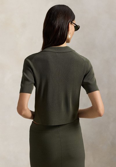 Κοντομάνικο, cropped τοπάκι σε σκούρο ελαιδί πράσινο ριμπ πλεκτό με γιακά πόλο. Διαθέτει λεία υφή και εφαρμοστή σιλουέτα.