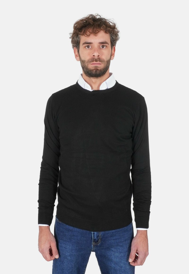 Maglione nero lavorato a maglia con scollo rotondo, maniche lunghe e polsini a coste, indossato sopra una camicia bianca con colletto, abbinato a jeans blu.