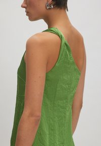 Grünes Kleid aus strukturiertem, zerknittertem Stoff, mit einem schulterfreien Design und verdrehten Trägerdetails. Saubere Linien und minimalistische Form.