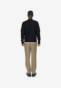 Schwarzer Strickpullover mit rundem Ausschnitt, kombiniert mit beigen, schmal zulaufenden Hosen und schwarzem Schuhwerk. Die Rückansicht zeigt eine lockere Passform und Textur.