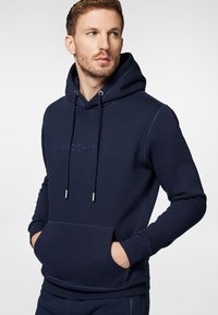 Granatowy hoodie wykonany z miękkiego materiału, z kieszenią na przodzie, kapturem na sznurku oraz wytłoczonym logo "PROCHNI" na klatce piersiowej.