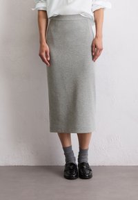 Šedá tužková sukně sahající po kolena, vyrobená z měkkého materiálu; má hladký povrch, boční švy a přiléhavý pas. Noste s černými mokasíny a šedými ponožkami.