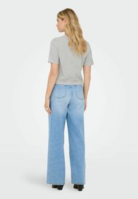 T-shirt a maniche corte grigio chiaro abbinato a jeans a gamba larga azzurri a vita alta, con tasche posteriori e sottili dettagli strappati.