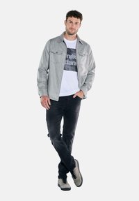 Gray long-sleeve shirt with two chest pockets, layered over a white graphic t-shirt, paired with black jeans and gray sneakers.