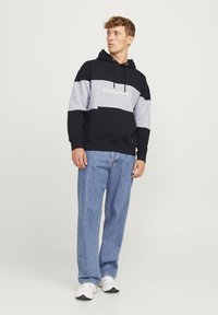 Hættetrøje i marineblå og grå farveblok med hvidt logo. Materiale af bomuldsblanding, afslappet pasform. Sammen med lyseblå denimjeans.