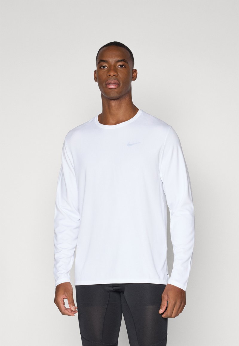 White long-sleeve athletic shirt with round neckline. Features a subtle blue Nike logo on the chest. Smooth, lightweight fabric.