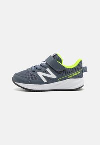 Chaussure de sport en maille bleue avec un logo blanc sur le côté, des accents vert fluo, une sangle ajustable, et une semelle noire avec un motif texturé.