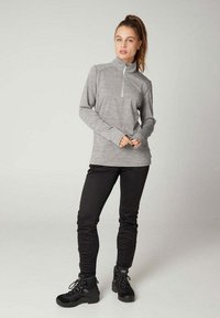 Graues Langarmoberteil mit einem Halb-Reißverschluss-Kragen, kombiniert mit schwarzen Hosen und schwarzen Stiefeln. Das Oberteil hat einen strukturierten Stoff und eine figurbetonte Passform.