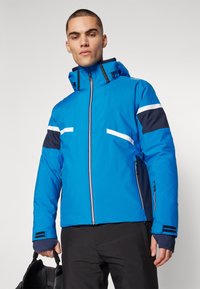 Helle blaue Skijacke mit hohem Kragen, weißen und marineblauen Akzenten, Reißverschluss vorne und zwei seitlichen Taschen. Glattes Material und dicke Isolation.