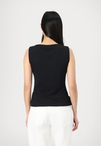Haut sans manches noir avec une texture côtelée et un col rond, associé à un pantalon blanc avec des poches arrière.