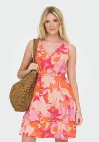 Vestido floral con escote en V, en tonos de rosa, naranja y durazno. Tejido fluido con cintura elástica, acompañado de un bolso de paja tejido.