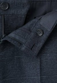 Donker wollen blazer met een gestructureerde stof, twee knopen, een ritszak en een gestikte voering. Subtiel geruit patroon zichtbaar.