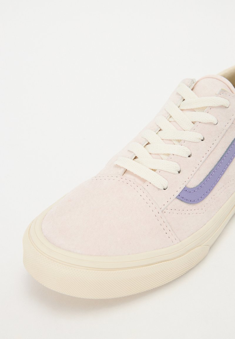 Zapatillas de ante color rosa claro con una suela de goma crema, que cuentan con cordones blancos planos y una rayita de acento púrpura a lo largo del costado.