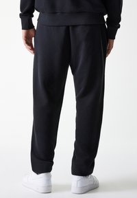 Schwarze Sweatpants aus weichem Stoff, mit einer lockeren Passform, gerippten Bündchen und Seitentaschen, kombiniert mit weißen Sneakers.