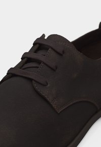 Κοντινό πλάνο σκούρου καφέ δερμάτινου παπουτσιού με κορδόνια, με ορατή ραφή και στρογγυλά κορδόνια, παρουσιάζεται σε λευκό φόντο.