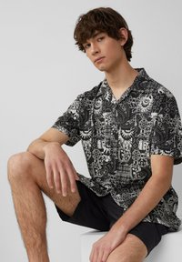 Korte mouw shirt in zwart-wit bloemenpatroon, met knoopsluiting, ontspannen pasvorm, lichtgewicht stof, gecombineerd met zwarte shorts.