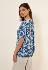 Blusa blu a motivo con maniche corte, scollo arrotondato e orlo arricciato. Presenta un design astratto tie-dye in diverse tonalità.