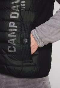 Gilet invernale nero con dettagli grigi e logo; dispone di una tasca con chiusura a pressione e polsini a coste; texture liscia e trapuntata.