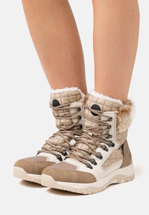 Bottes imperméables beige et crème avec texture matelassée, doublure en fausse fourrure et accents en daim marron. Elles présentent des lacets épais et une semelle durable.