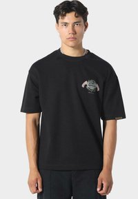 Sort bomulds t-shirt med korte ærmer, der har et farverigt broderet grafisk motiv på brystet og et lille mærketag på siden.