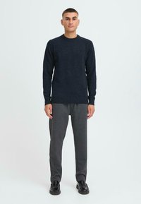 Navyfarbener Wollpullover mit rundem Halsausschnitt, gerippten Bündchen und Saum. Dazu dunkelgraue Jogginghose und schwarze Schuhe.