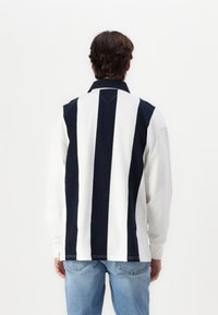 Long-sleeve polo shirt featuring navy and white vertical stripes, a collar, and contrasting stitching. Casual fit with a back pleat detail.