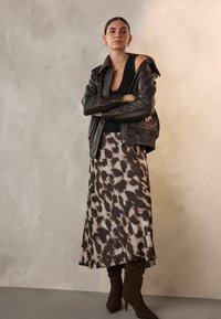 Schwarze Lederjacke mit einem braunen Kunstfellkragen, kombiniert mit einem beigen Satinrock im Leopardenmuster und braunen Stiefeln mit hohen Absätzen bis zum Oberschenkel.