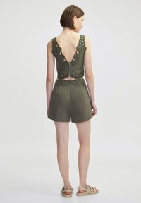 Top corto sin mangas en verde oliva con espalda baja y borde de encaje texturizado, combinado con pantalones cortos de talle alto a juego.